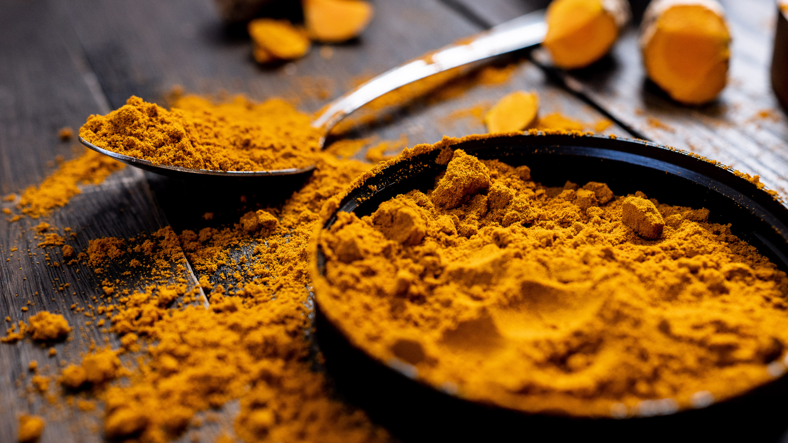 Un plat remplie de curcuma, posé sur une table ancienne.